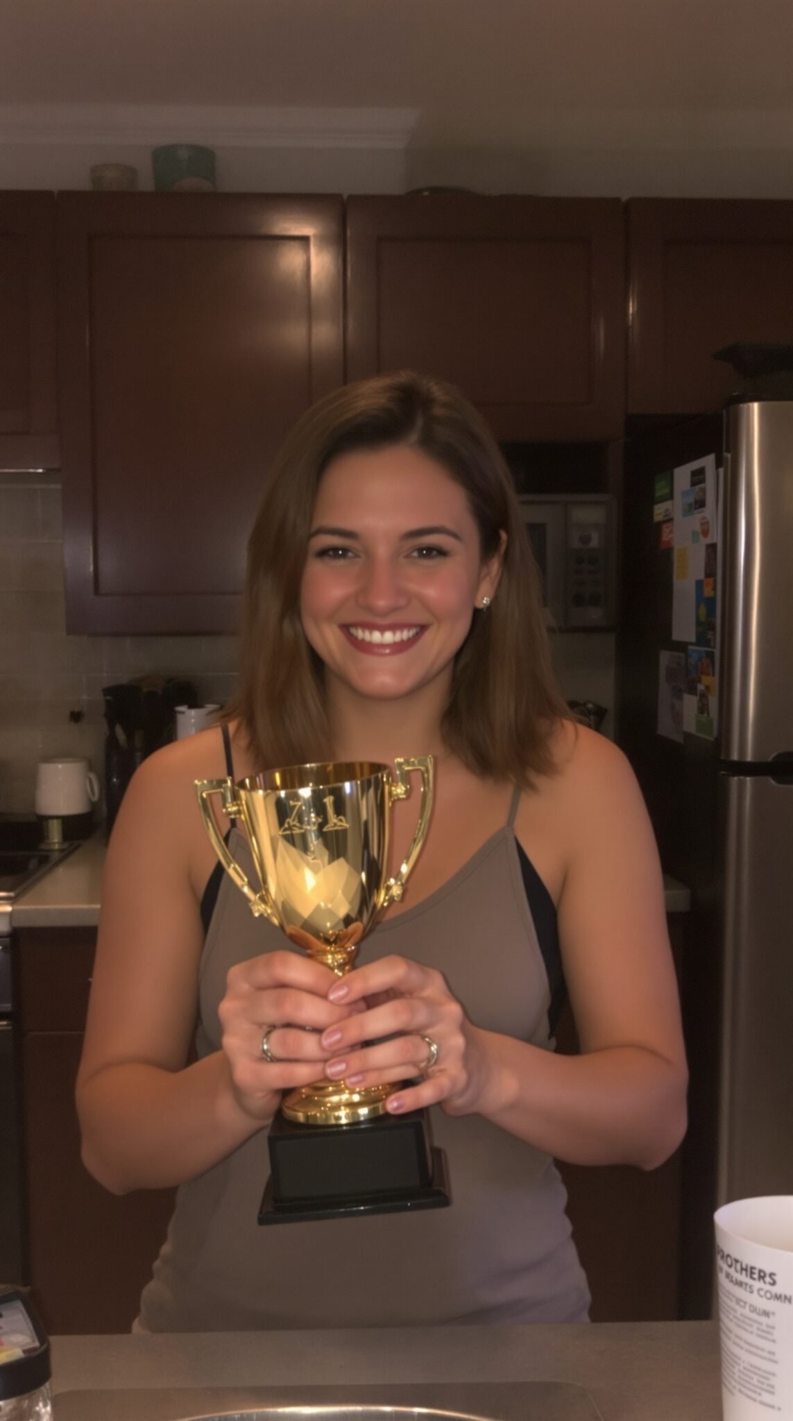 A smiling woman holding a gold trophy in a kitchen