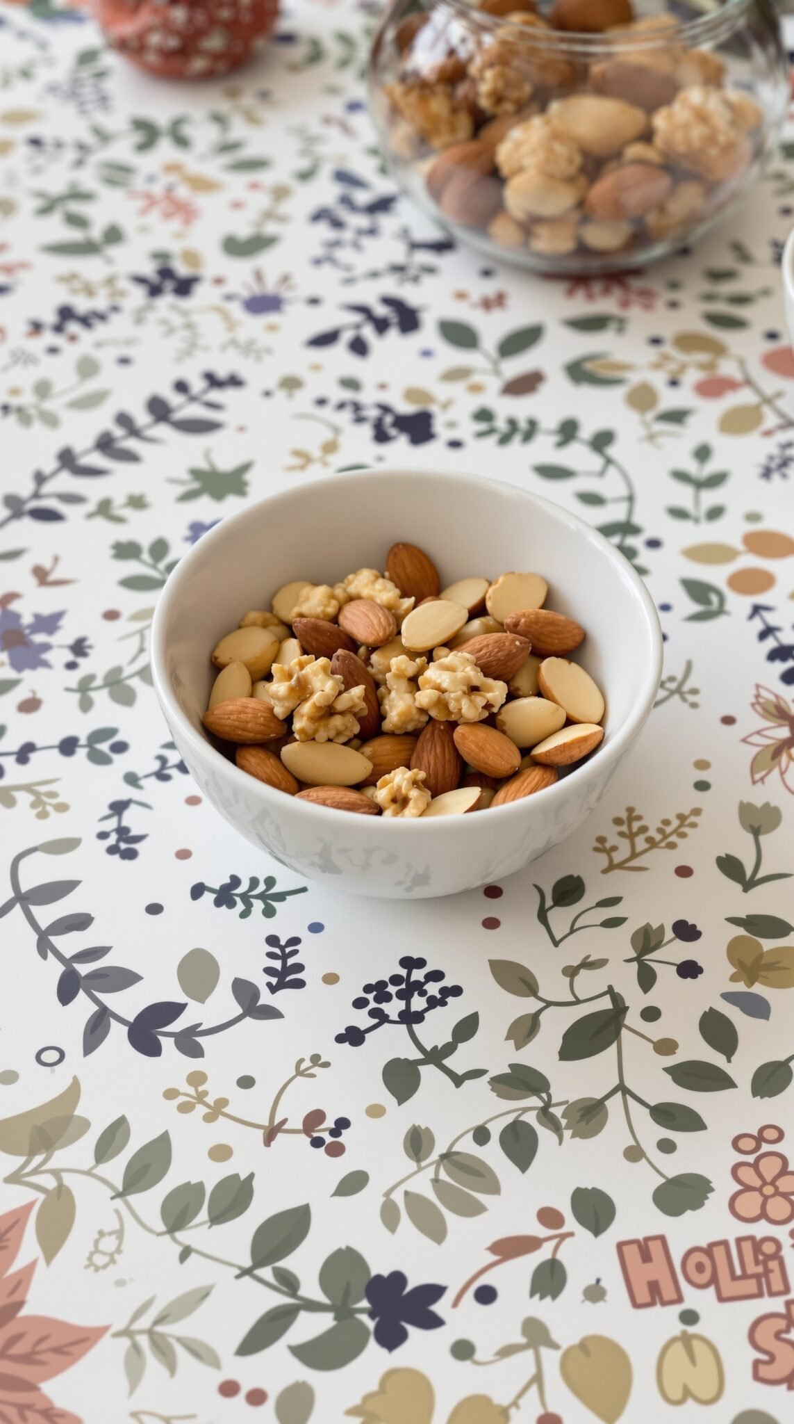 A bowl filled with almonds and walnuts on a decorative floral tablecloth