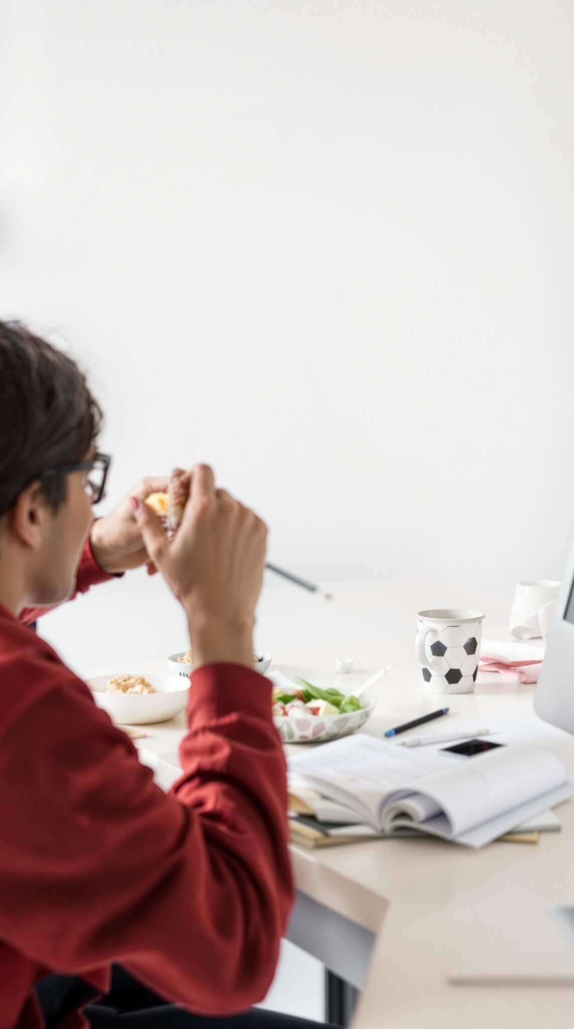 Person eating a sandwich at a table filled with food and study materials.